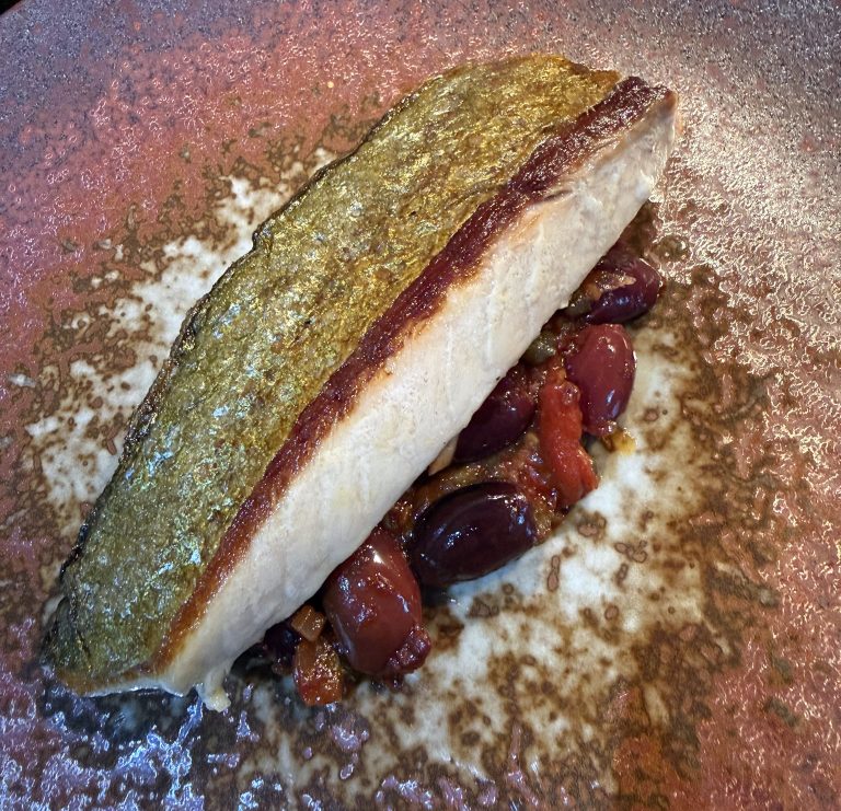 Skin-on trevally fillet pan-seared to a crisp golden finish, served on a dark oxidised ceramic plate over a Provençal sauce of kalamata olives and slow-cooked tomato.