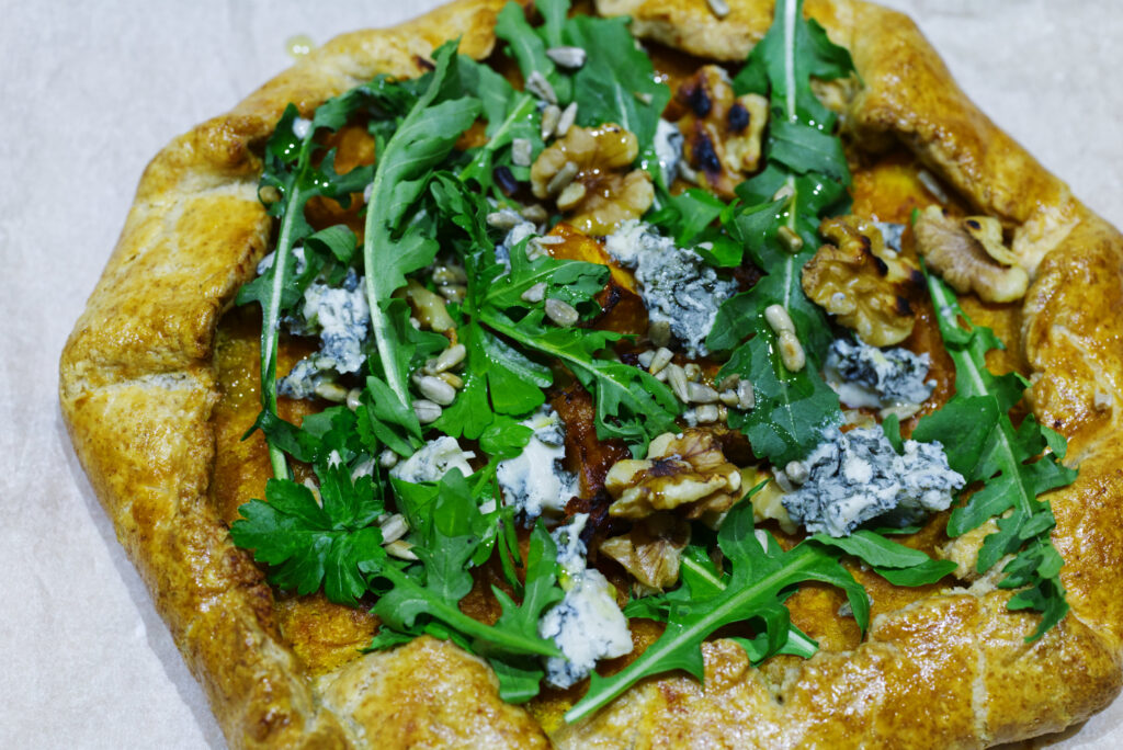Roasted pumpkin galette straight from the oven, finished with blue cheese, walnuts, sunflower seeds and rocket