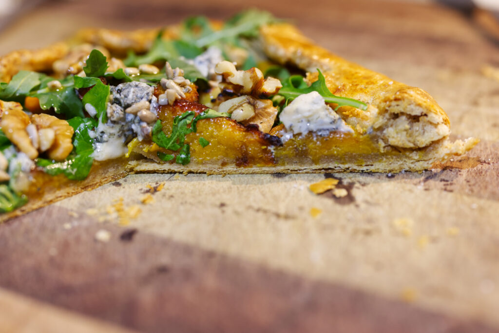 Cross-section of a rustic pumpkin galette showing the roasted pumpkin filling against buttery pastry, topped with blue cheese, walnuts and rocket